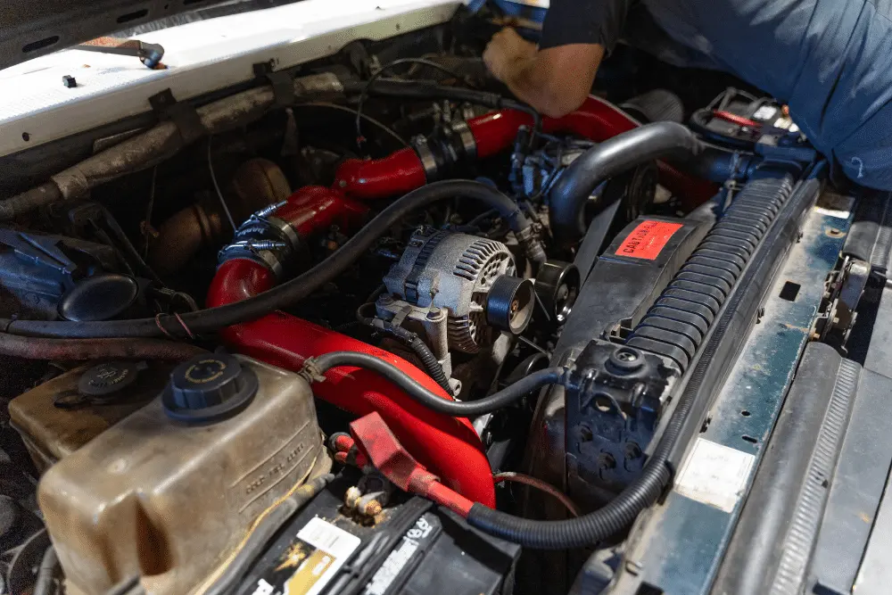 diesel repair in Brooksville, FL at RDI Power. A mechanic works on a truck engine bay featuring bright red aftermarket intake piping, an alternator in the center, a radiator at the front, and a coolant reservoir to the left.