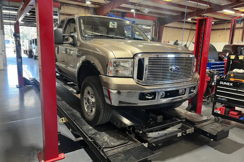 diesel truck, diesel repair in Brooksville, FL at RDI Power. Beige Ford Super Duty pickup truck positioned on a wheel alignment lift inside a well-equipped auto repair shop.