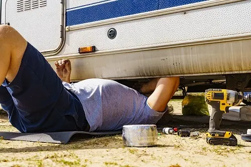 Does an RV Break Down a Lot? | RDI Power in Brooksville, FL. Image of a man lying on ground, repairing the bottom of an RV.