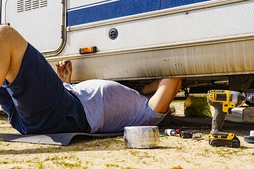 Does an RV Break Down a Lot? | RDI Power in Brooksville, FL. Image of a man lying on ground, repairing the bottom of an RV.